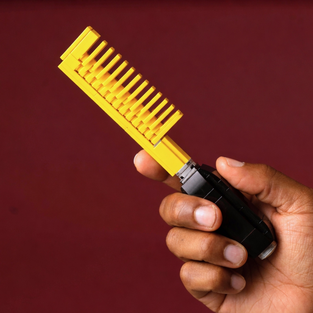 Hand holding a yellow and black hairbrush against a red background made of lego