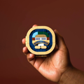 Hand holding a small round object with a design on a brown background