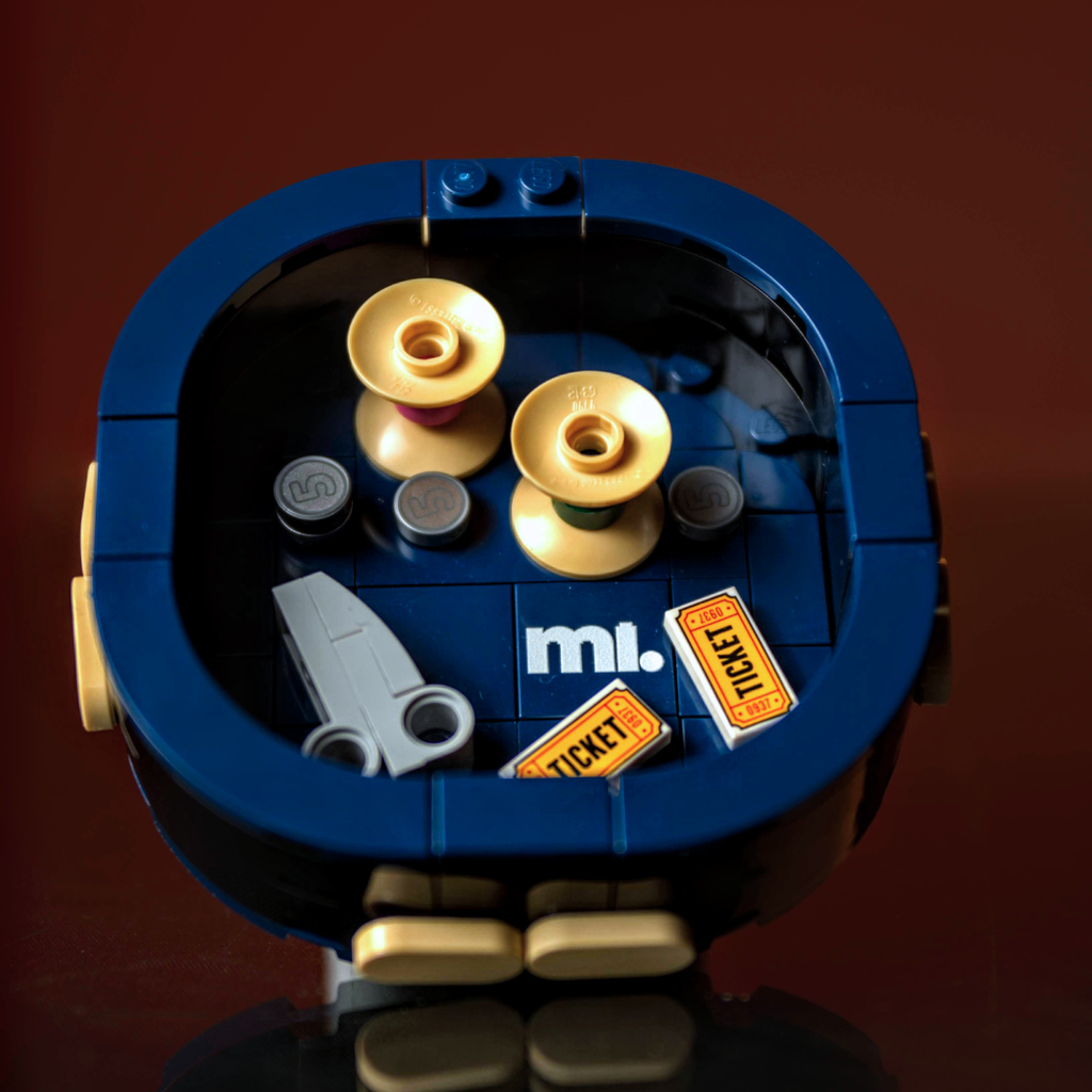 Close-up of a LEGO piece with blue border, gold elements, and 'mi.' branding on a dark background.