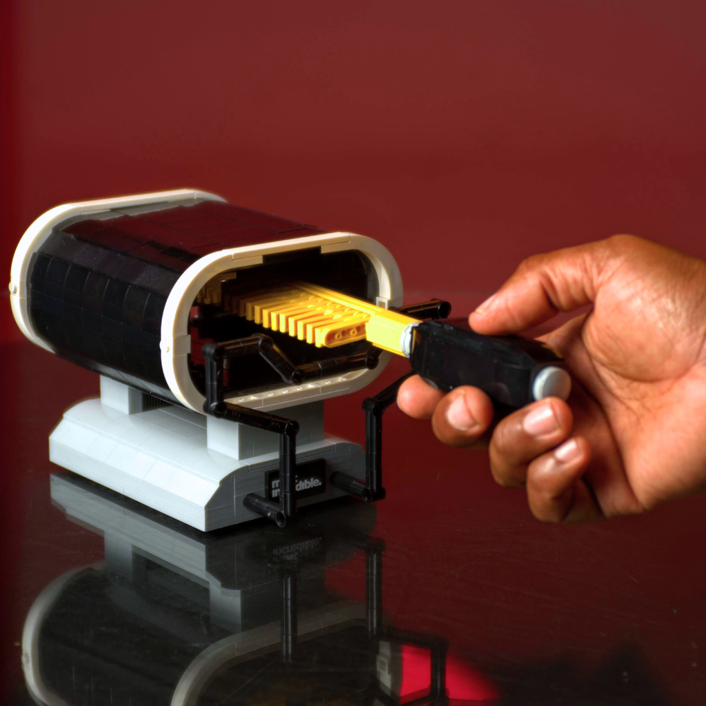 Hand using a tool to open a small electronic device on a reflective surface with a red background Lego