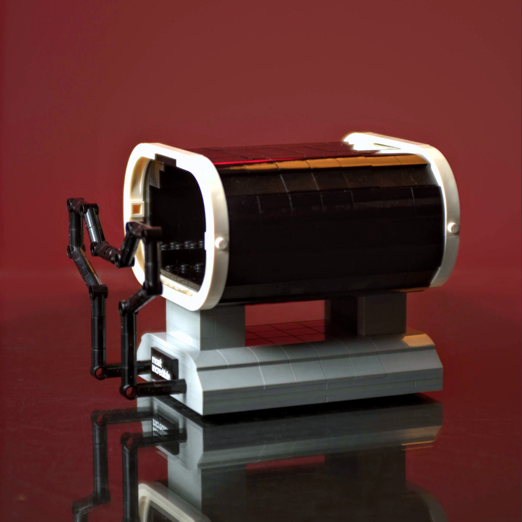 Toy robot with a cylindrical body and mechanical arm on a reflective surface with a red background Made of Lego